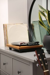 Stylish turntable with vinyl record on chest of drawers indoors