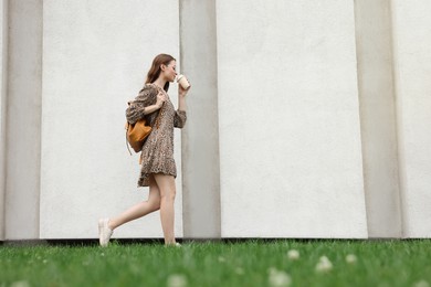 Young woman with cup of drink walking near stone wall outdoors, space for text