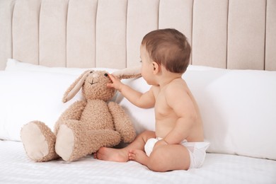 Cute baby in dry soft diaper with toy bunny on white bed at home