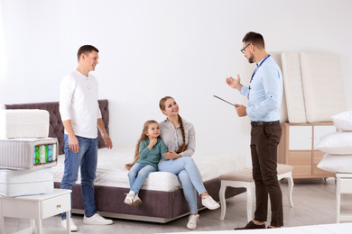 Photo of Salesman consulting couple with child at mattress store