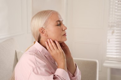 Mature woman doing thyroid self examination at home, space for text