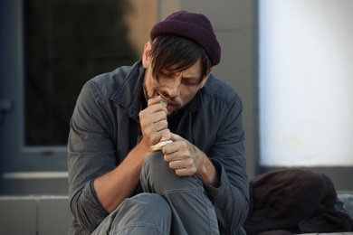 Poor homeless man eating piece of bread on city street