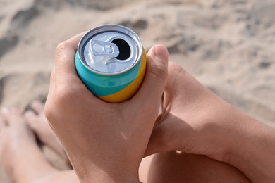 Photo of Woman holding aluminum can with beverage on sand, closeup