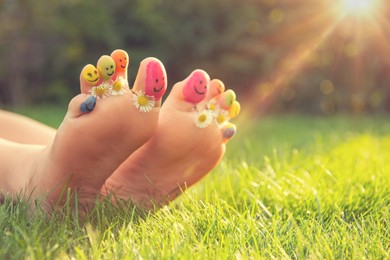 Teenage girl with drawn smiling faces and chamomiles between toes outdoors, closeup. Space for text