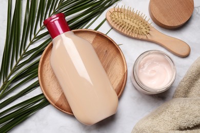 Photo of Bottle of shampoo, cream and hairbrush on white marble table, flat lay