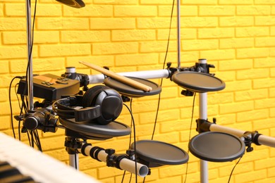 Modern electronic drum kit near yellow brick wall indoors. Musical instrument