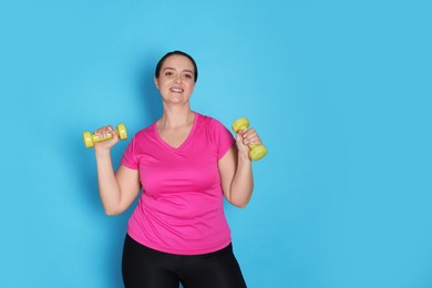 Happy overweight woman doing exercise with dumbbells on light blue background, space for text