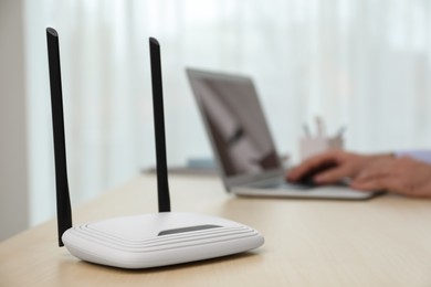 Man working with laptop in office, focus on router. Wireless internet communication