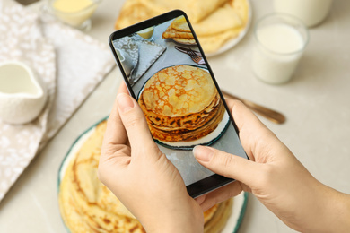 Blogger taking photo of thin pancakes at table, closeup