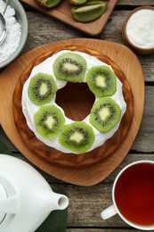 Photo of Homemade yogurt cake with kiwi, cream and aromatic tea on wooden table, flat lay