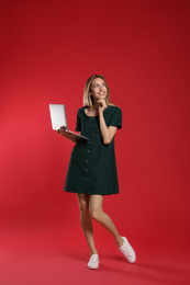 Full length portrait of happy woman with modern laptop on red background