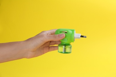 Photo of Woman holding electric vaporizer with insect repellent liquid on yellow background, closeup