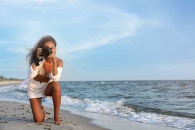 African American photographer taking photo with professional camera near sea