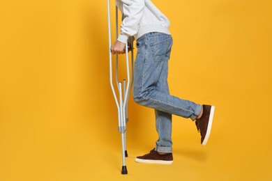 Man with injured leg using crutches on yellow background, closeup