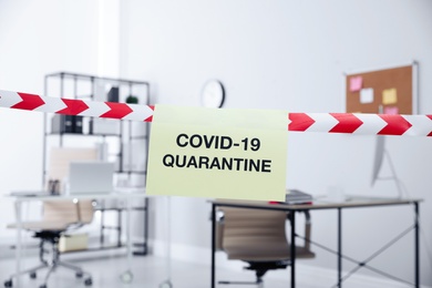 Photo of Sheet of paper with words COVID-19 Quarantine on red and white tape in office