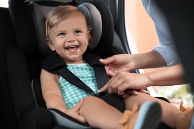 Mother fastening her daughter in child safety seat inside car