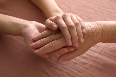 Young and elderly women holding hands together on pink fabric, closeup
