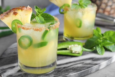 Photo of Glasses of spicy pineapple cocktail with jalapeno and mint on grey table, closeup. Space for text