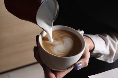 Barista pouring steamed milk from pitcher into cup of aromatic coffee in cafe, closeup