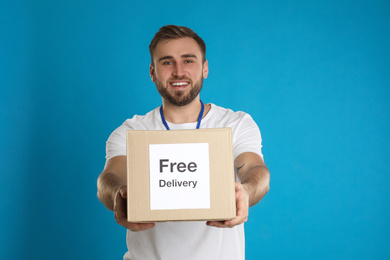 Male courier holding parcel with sticker Free Delivery on light blue background