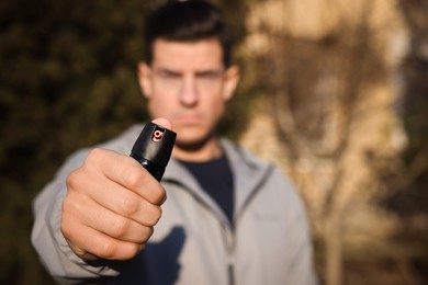 Man using pepper spray outdoors, focus on hand. Space for text