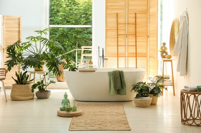 Photo of Stylish bathroom interior with modern tub, window and beautiful houseplants. Home design