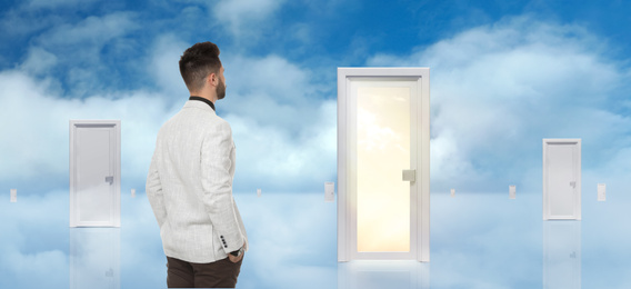 Young man standing in front of many doors against blue sky. Choice concept