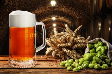 Image of Glass of tasty beer, fresh hops and wheat spikes on wooden table in cellar