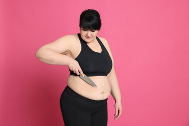 Obese woman with knife and marks on body against pink background. Weight loss surgery