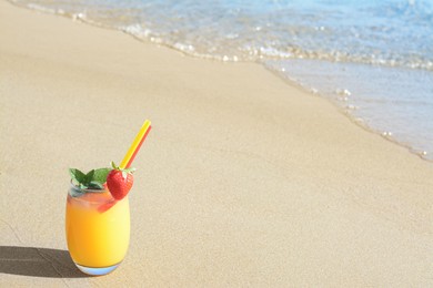 Glass of refreshing drink with strawberry on sandy beach near sea, space for text