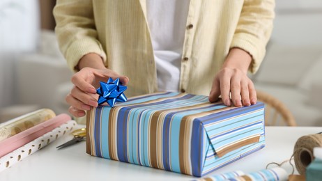Woman wrapping gift at white table indoors, closeup