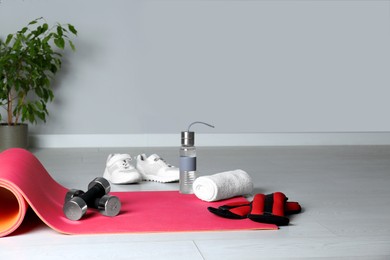Photo of Exercise mat and other sport equipment on light wooden floor indoors