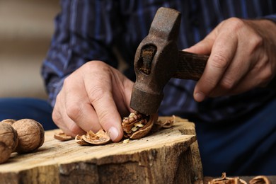 Man cracking walnuts with hammer at table, closeup