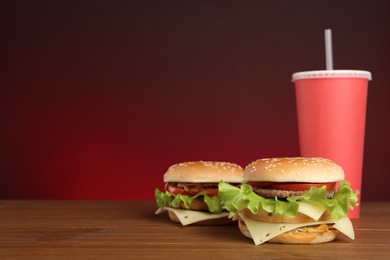 Photo of Delicious burgers and drink on wooden table against red background, space for text. Fast food menu