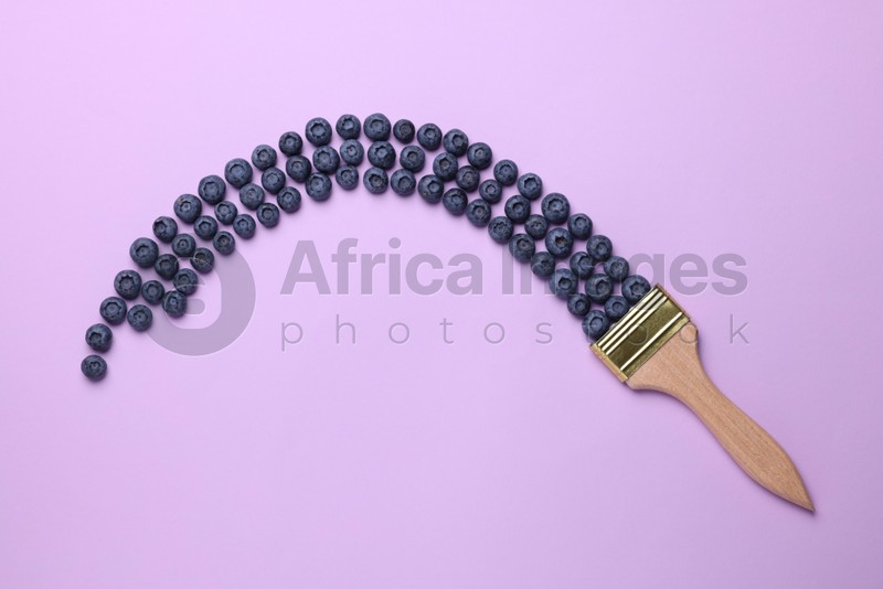 Creative flat lay composition with paint brush and blueberries on violet background