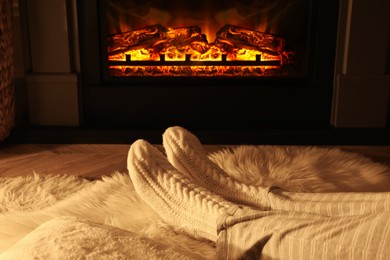 Photo of Woman in knitted socks resting near fireplace at home, closeup of legs