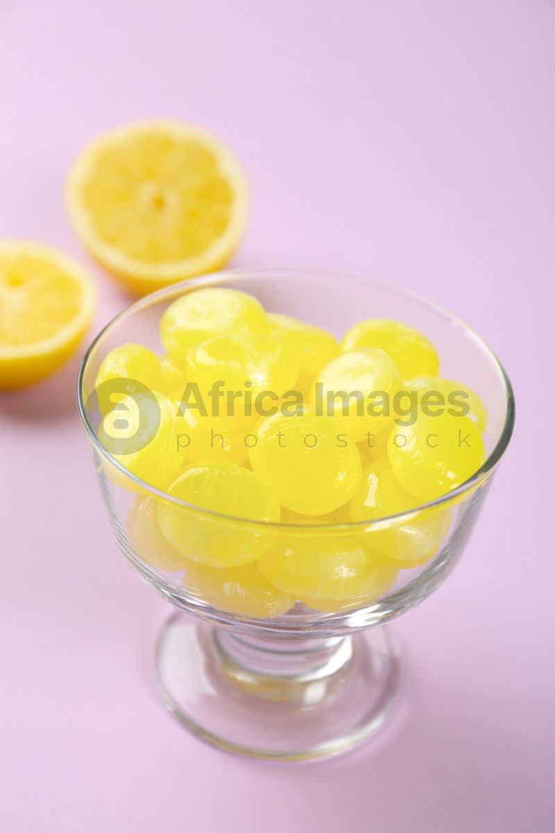 Tasty lemon drops in dessert bowl on violet background