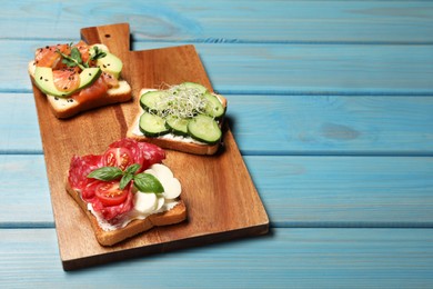 Photo of Tasty toasts with different toppings served on light blue wooden table. Space for text