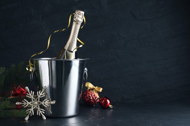 Happy New Year! Bottle of sparkling wine in bucket and festive decor on black background, space for text