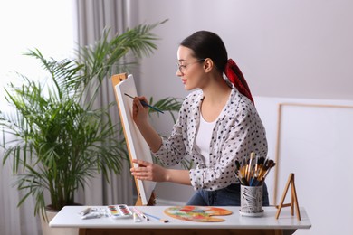 Happy woman artist drawing picture on canvas in studio