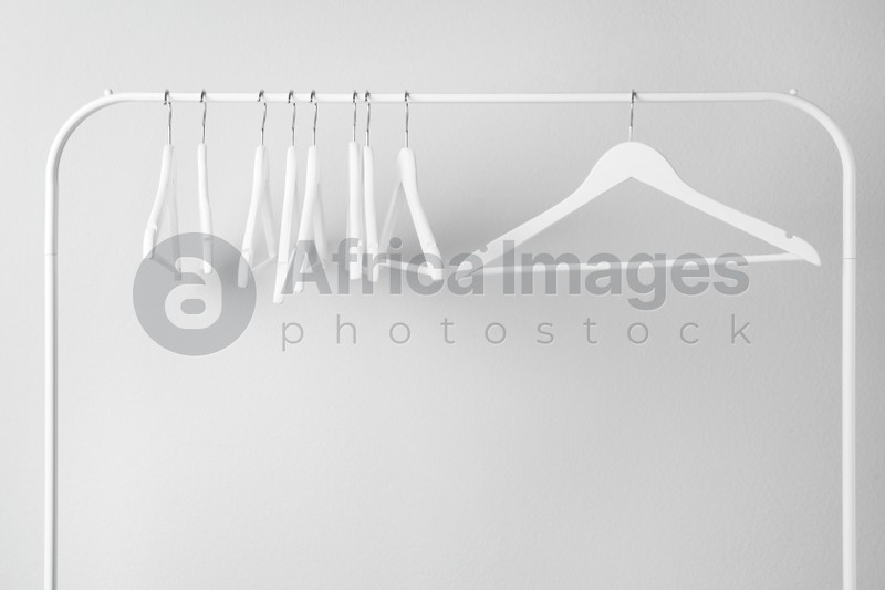 Photo of White clothes hangers on metal rack against light grey background