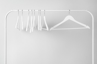 White clothes hangers on metal rack against light grey background