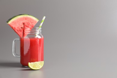 Photo of Tasty summer watermelon drink with lime in glass mason jar on grey background. Space for text