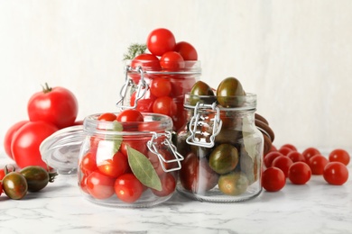 Pickling jars with fresh ripe tomatoes on white marble table
