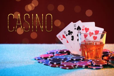 Word Casino, chips, playing cards and glass of alcohol on table against red background with blurred lights. Bokeh effect