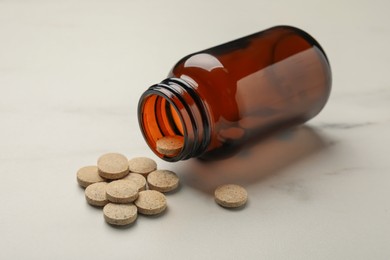 Overturned bottle with dietary supplement pills on white table