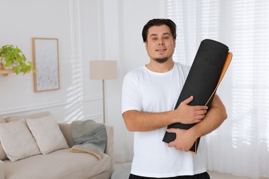 Overweight man with yoga mat at home, space for text