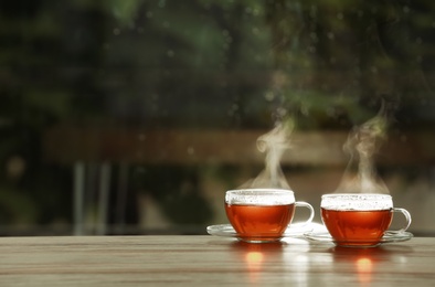 Cups of hot tea on wooden table against blurred background, space for text