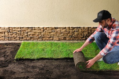 Young man laying grass sod on ground at backyard, space for text