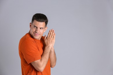 Greedy man rubbing hands on grey background, space for text
